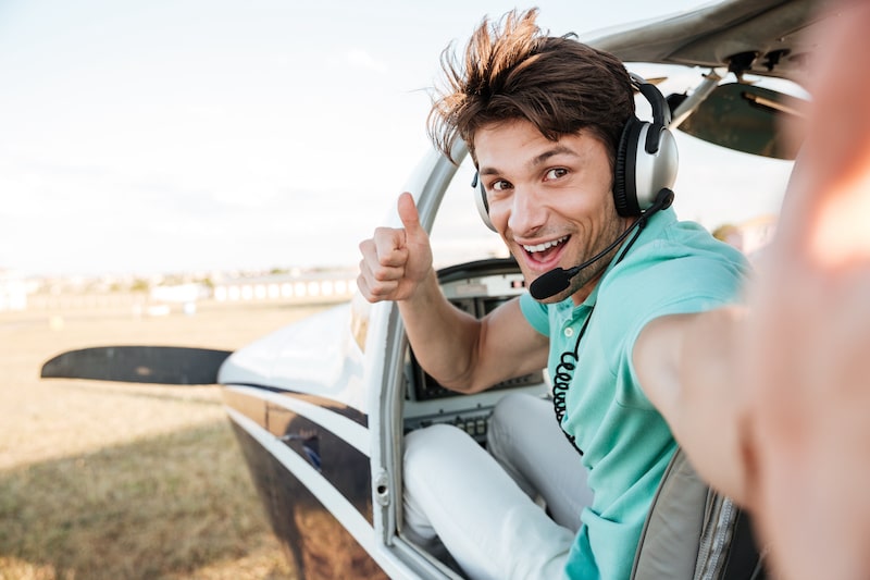 A young pilot sitting in his small plane gives thumbs up.